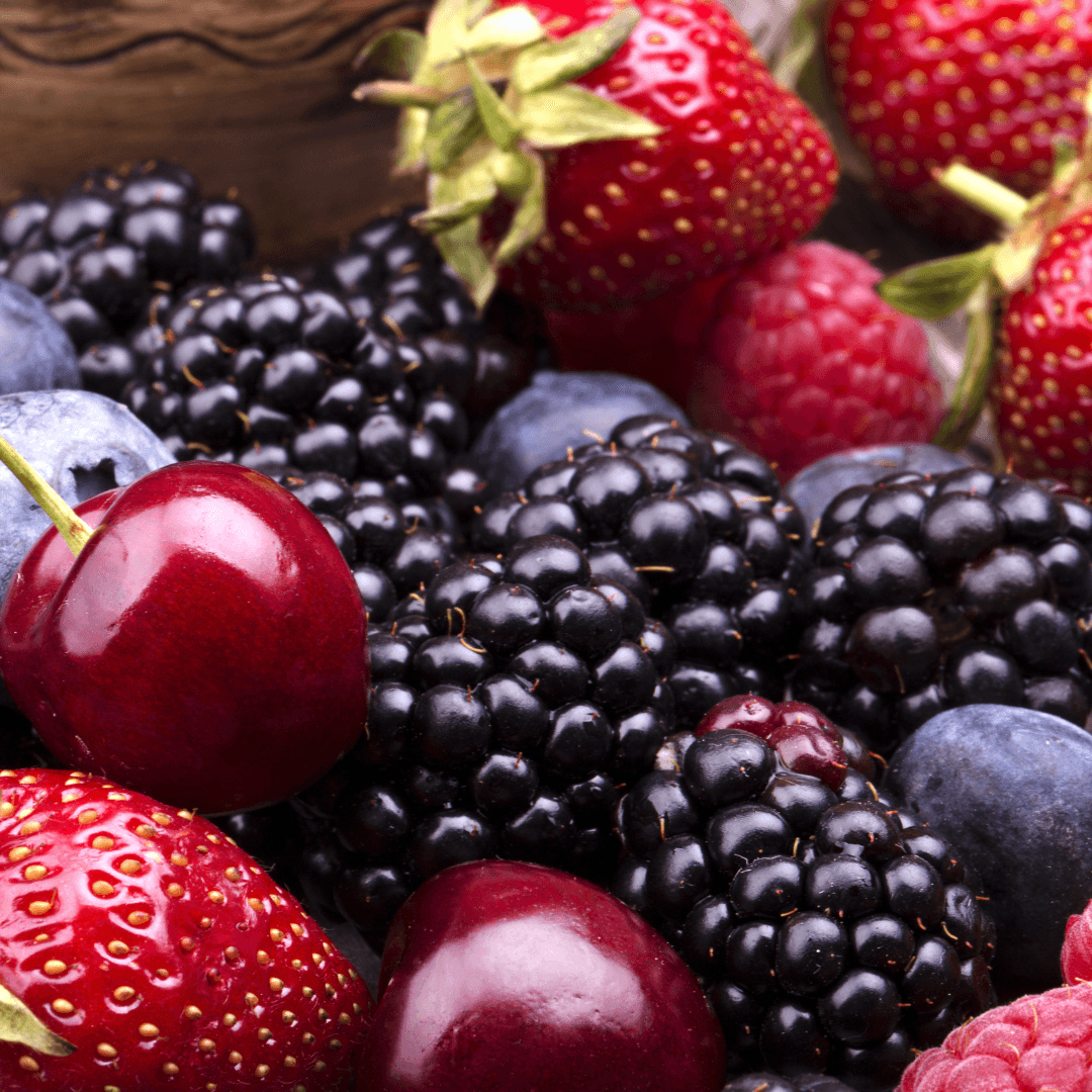 Colourful arrangement of fresh berries including red strawberries, dark blackberries, red cherries, blueberries, and raspberries on a wooden surface