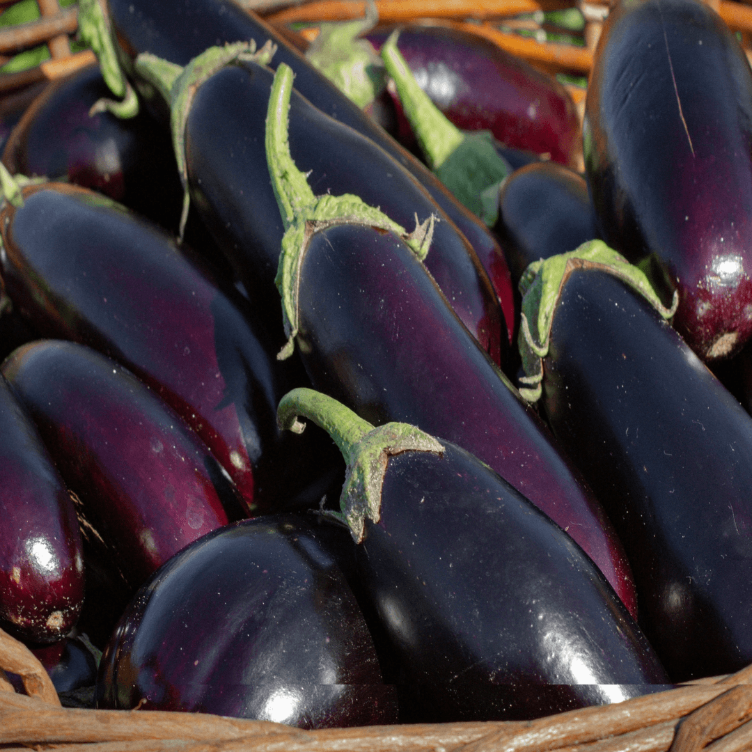 A collection of fresh, glossy dark purple aubergines with green stems arranged in a wooden crate at a market or farm stall.