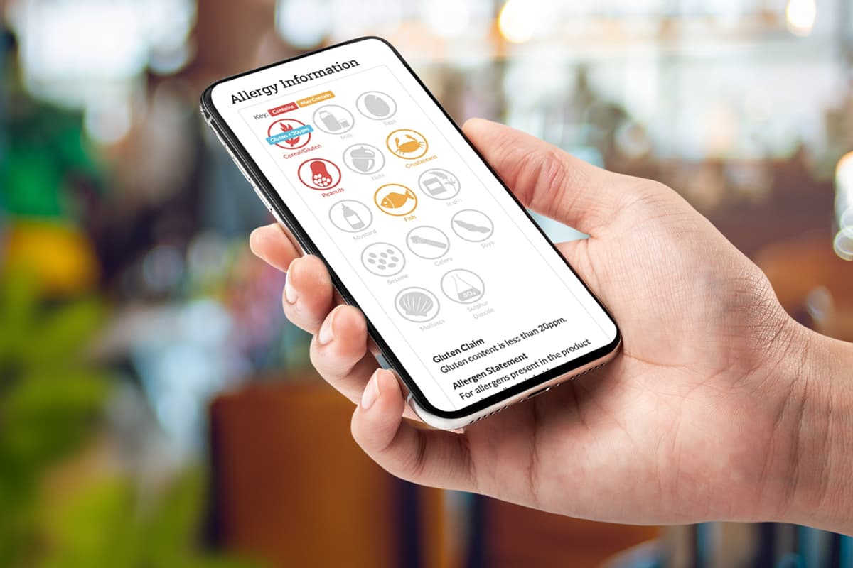 Smartphone displaying an allergy information screen with various allergen icons including gluten, crustaceans, molluscs, fish, peanuts, tree nuts, celery, mustard, sesame, sulphites, lupin, and molluscs, along with a gluten claim statement.