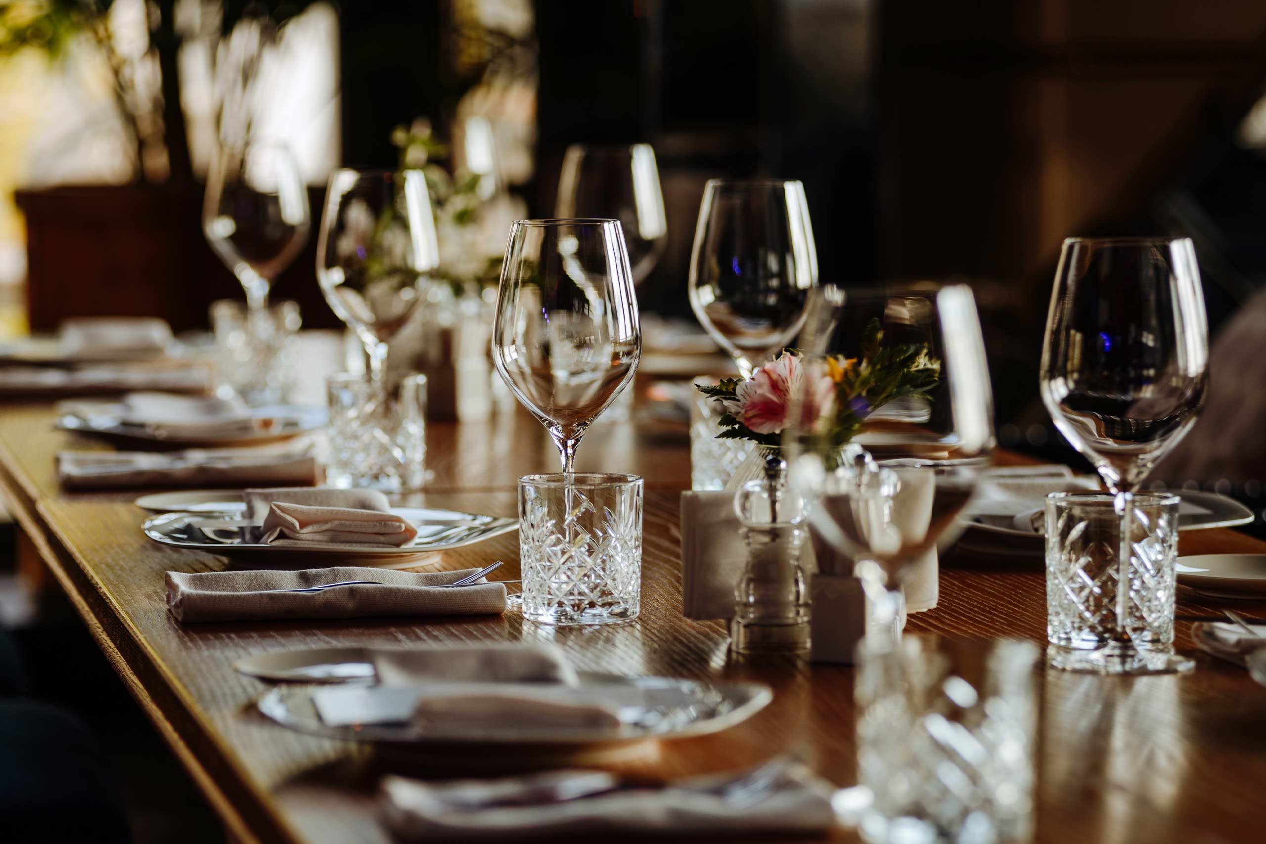 An elegantly set dining table featuring crystal wine glasses, polished cutlery, cloth napkins, and small floral arrangements in a formal restaurant setting.