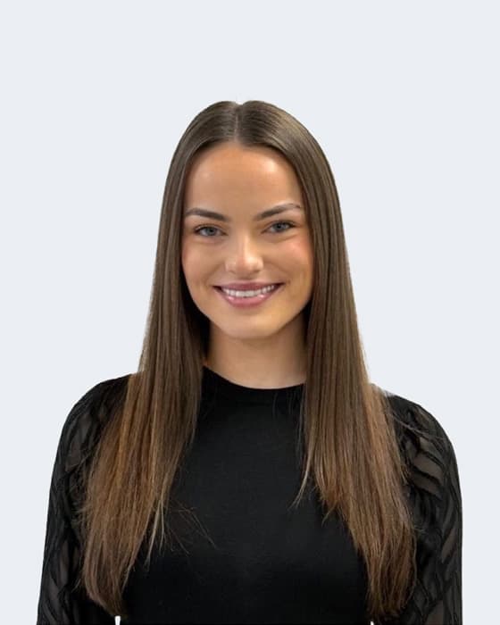 Professional headshot of a smiling woman with long brown hair wearing a black top against a white background.