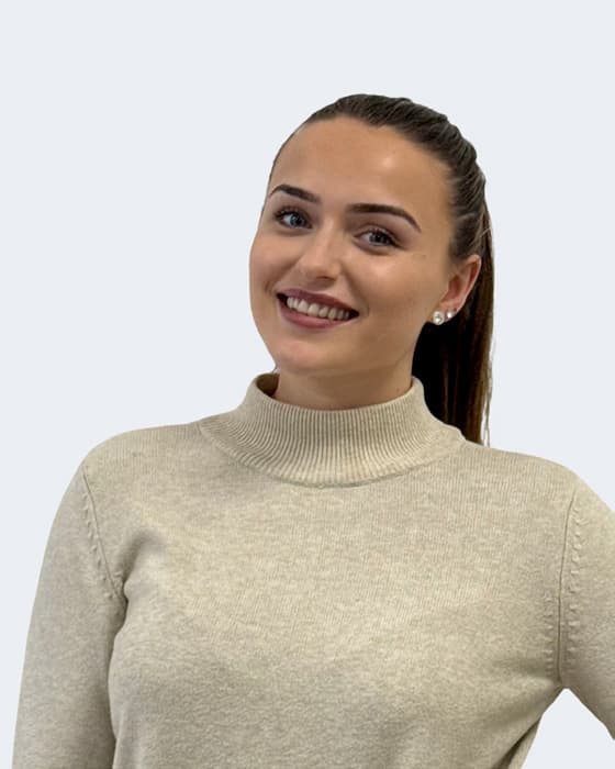 Professional headshot of a woman with long dark hair wearing a beige turtleneck jumper, smiling against a white background.