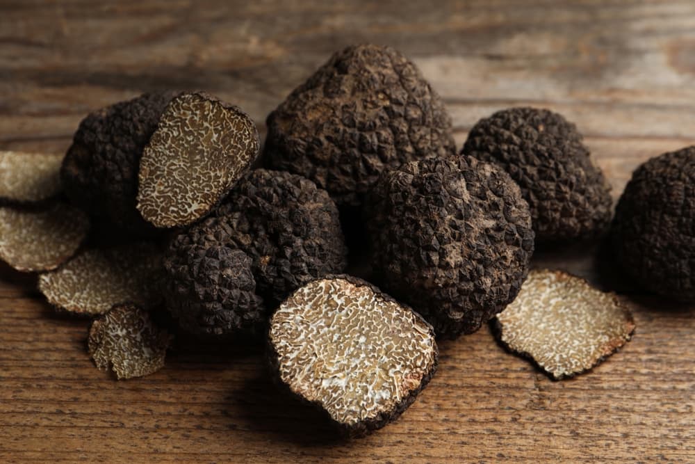 Whole and sliced black and white truffles arranged on a rustic wooden background, showcasing their distinctive textured exterior and pale interior.