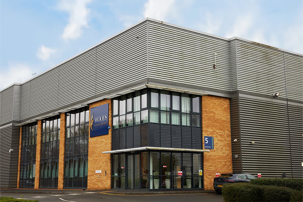 Modern warehouse facility with corrugated metal cladding, brick entrance section, and blue signage bearing the Woods logo and unit number 5.