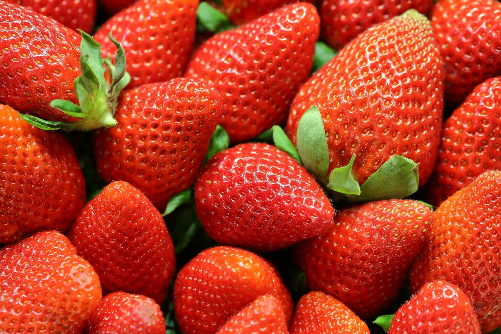 Close-up photograph of ripe red strawberries with visible seeds and green leafy crowns, arranged tightly together